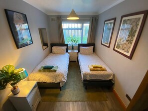 A room with two beds, a bedside table, a potted plant, and a window with curtains. - #06 Riverside Retreat| Near the NEC| Guest for 6 (Coleshill)