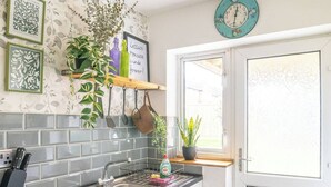 A kitchen with a tiled backsplash, hanging utensils, a window with a view, and decorative wall art. - #06 Riverside Retreat| Near the NEC| Guest for 6 (Coleshill)