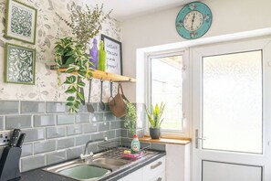 A kitchen with a tiled backsplash, hanging utensils, a window with a view, and decorative wall art. - #06 Riverside Retreat| Near the NEC| Guest for 6 (Coleshill)