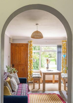 A cozy room with a wooden door, a blue sofa, a dining table with chairs, and a hanging light fixture. - #06 Riverside Retreat| Near the NEC| Guest for 6 (Coleshill)