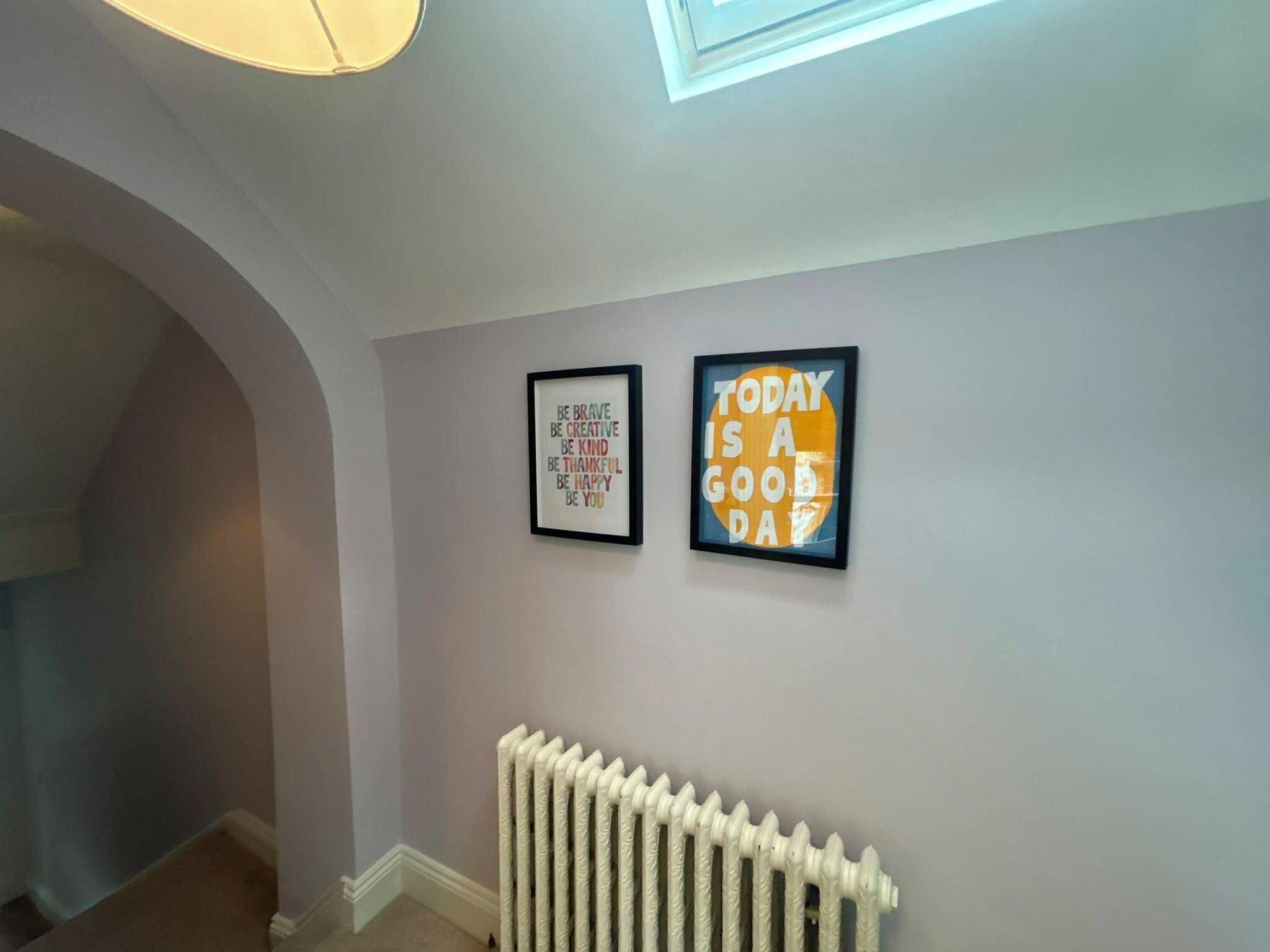 A hallway with a radiator, two framed inspirational quotes on the wall, and a skylight above.