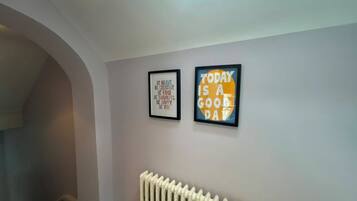 A hallway with a radiator, two framed inspirational quotes on the wall, and a skylight above.