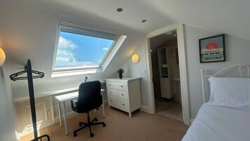 A bedroom with a bed, a desk, a chair, a window, and a door leading to another room.