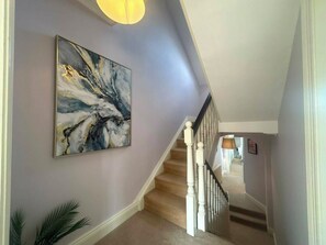 A hallway with a staircase, a painting on the wall, and a lamp. - Elegant 4BDR 4BA Luxury Home Heart of Rathmines (Dublin)