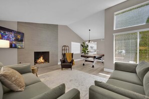 Una sala de estar moderna con chimenea, un comedor y una cocina al fondo.