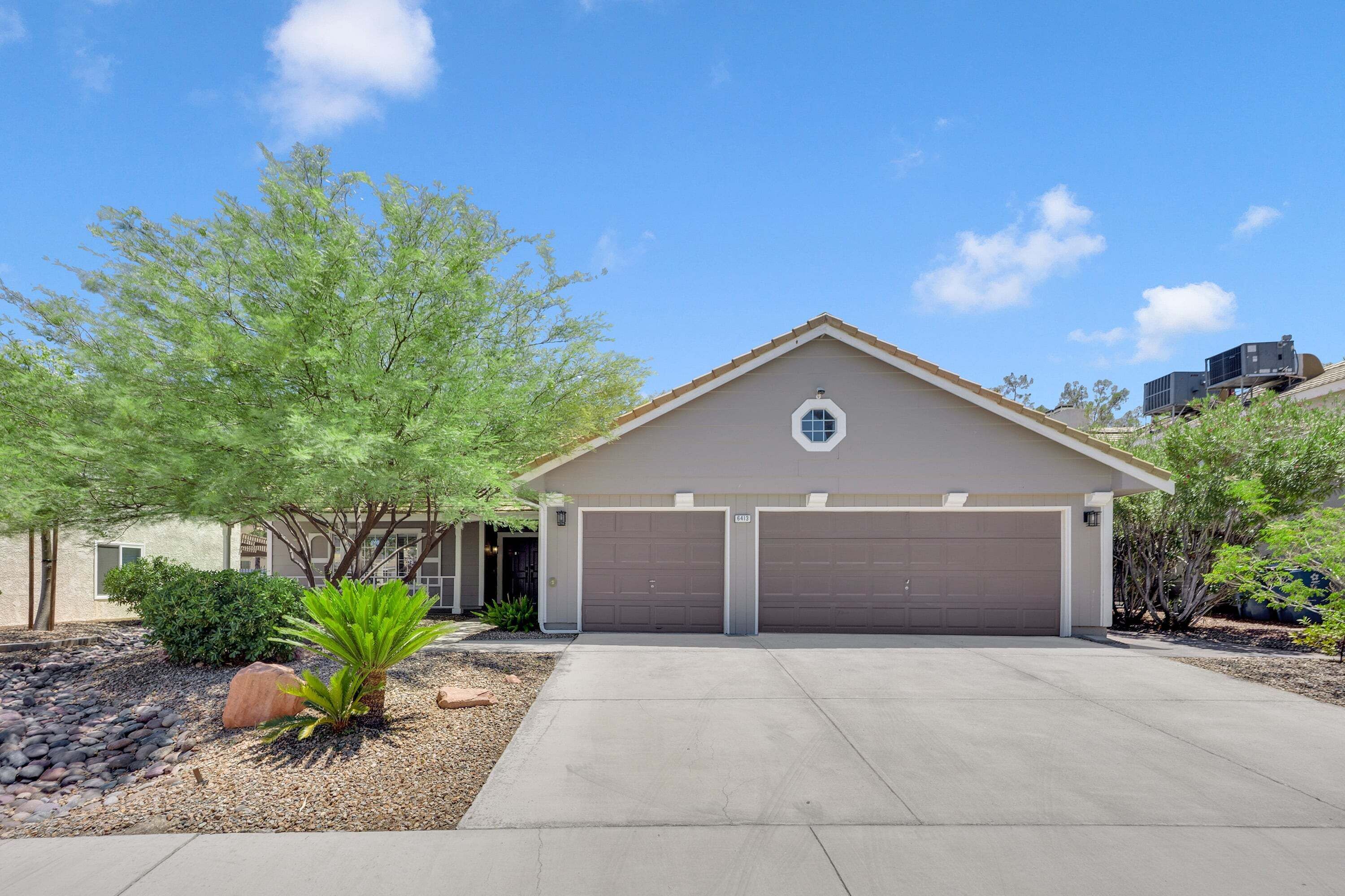 A single-story house with a garage, a small front yard with a palm tree, and a clear blue sky.