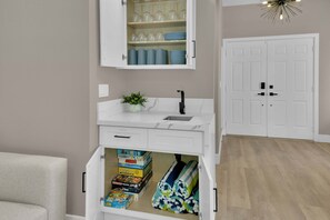 Un baño con tocador blanco, lavamanos y un mueble con cristalería y toallas.
