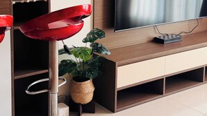 A modern living room with a flat-screen TV mounted on a wooden cabinet, a red bar stool, a small potted plant, and decorative items on the wall. - Green Valley EmHouse (Ho Chi Minh City)