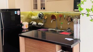 A kitchen with a black refrigerator, a black pendant light, a sink, and wooden cabinets. - Green Valley EmHouse (Ho Chi Minh City)