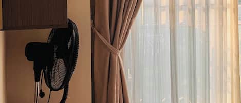 Quarto com um ventilador, uma estante e uma janela com cortinas leves.