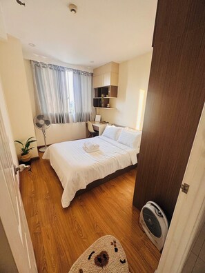 Habitación de hotel con cama, mesita de noche, escritorio, silla y un pequeño ventilador.