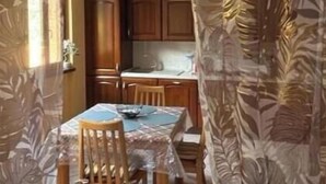 A dining area with a table and chairs, a kitchen in the background, and curtains with a leaf pattern. - NEW LarioView Suites – Apartment with Private Jacuzzi and Terrace with Lake Views (Argegno)
