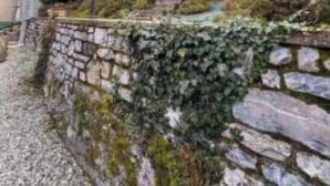 A stone retaining wall with vegetation, a paved area, and a building in the background. - NEW LarioView Suites – Apartment with Private Jacuzzi and Terrace with Lake Views (Argegno)