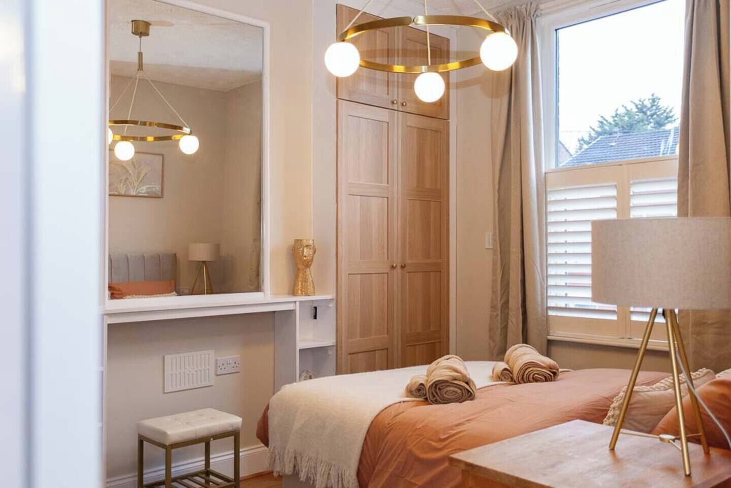 Une chambre à coucher avec un lit, un banc, un miroir, une armoire et une fenêtre avec des rideaux.