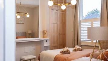Une chambre à coucher avec un lit, un banc, un miroir, une armoire et une fenêtre avec des rideaux.