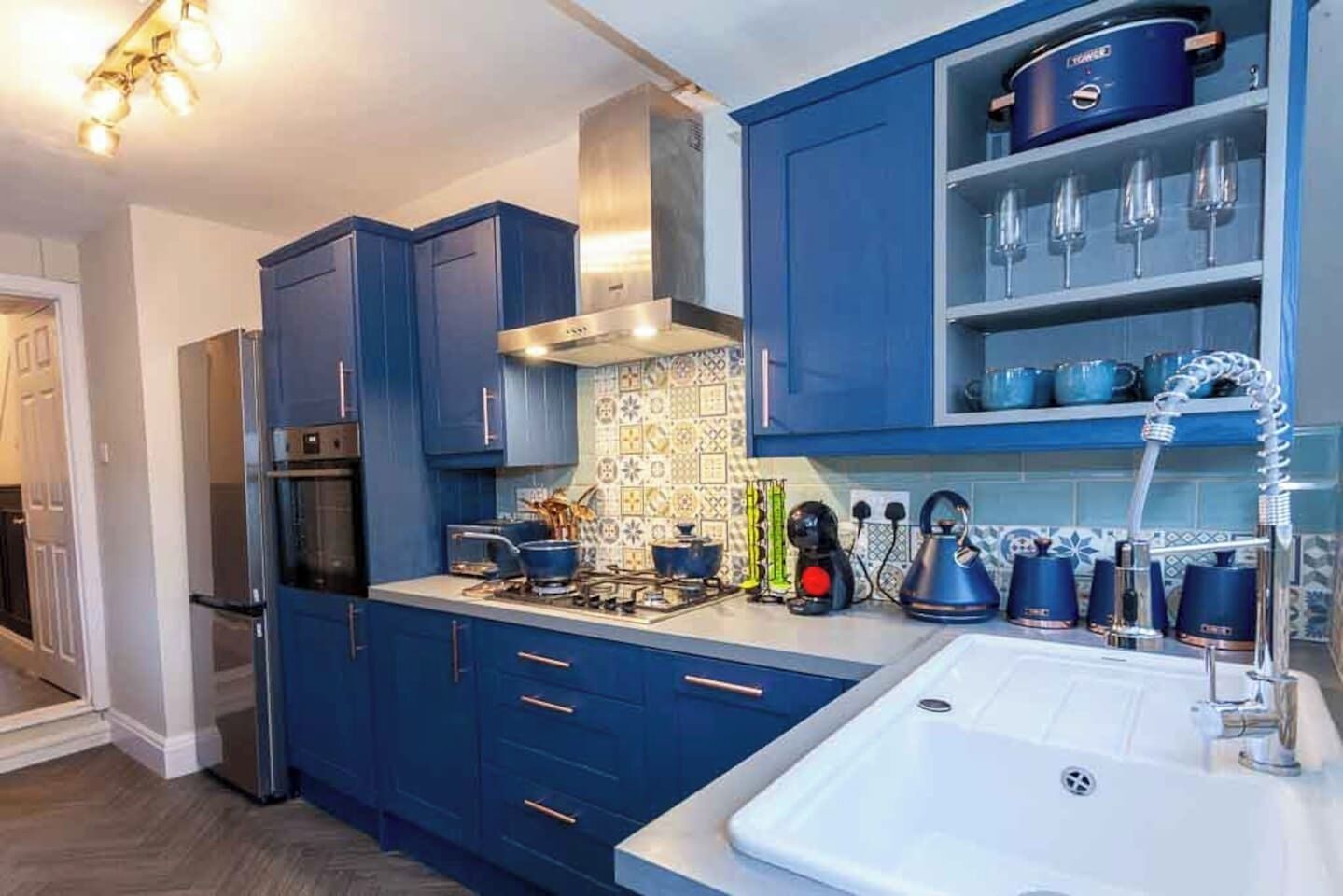 Une cuisine moderne avec des armoires bleues, une hotte de cuisinière en acier inoxydable et un meuble à vin intégré.