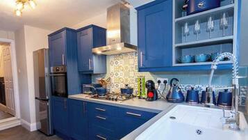 Una cocina moderna con armarios azules, una campana extractora de acero inoxidable y una estantería empotrada para vinos.