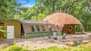 A rustic cabin with a sloped roof, a small attached shed, and a seating area with outdoor furniture.