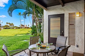 A patio with a table set for two, chairs, a bottle, and glasses. - Hawaiian Getaway | 1BR Walk to Beach (Kihei)