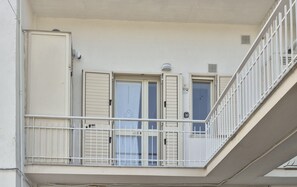 Ein Balkon mit weißer Brüstung, eine Tür mit Fensterläden und ein Fenster mit Vorhang.