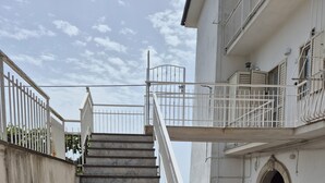 Um conjunto de degraus de concreto que levam a um edifício, com corrimão branco e portão de metal no topo.
