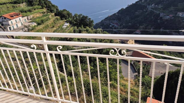 Uma varanda com vista para a paisagem costeira, incluindo uma estrada e edifícios.