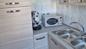 Uma cozinha moderna com armários de madeira clara, micro-ondas embutido, máquina de café e uma pia de aço inoxidável.