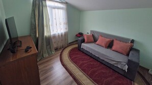 A room with a sofa, a television, and a desk. - cozy house with stunning views of the Aragvi Valley (Ananuri)