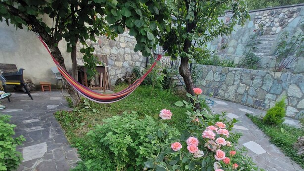 A stone pathway leading through a garden with pink roses and a hammock. - cozy house with stunning views of the Aragvi Valley (Ananuri)