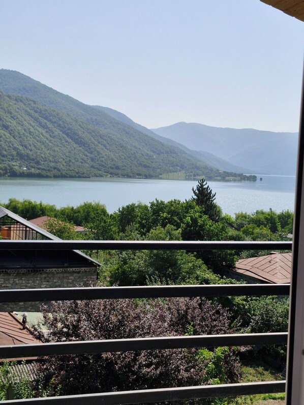 A view of a lake with mountains in the background, a balcony with a railing, and some greenery in the foreground.