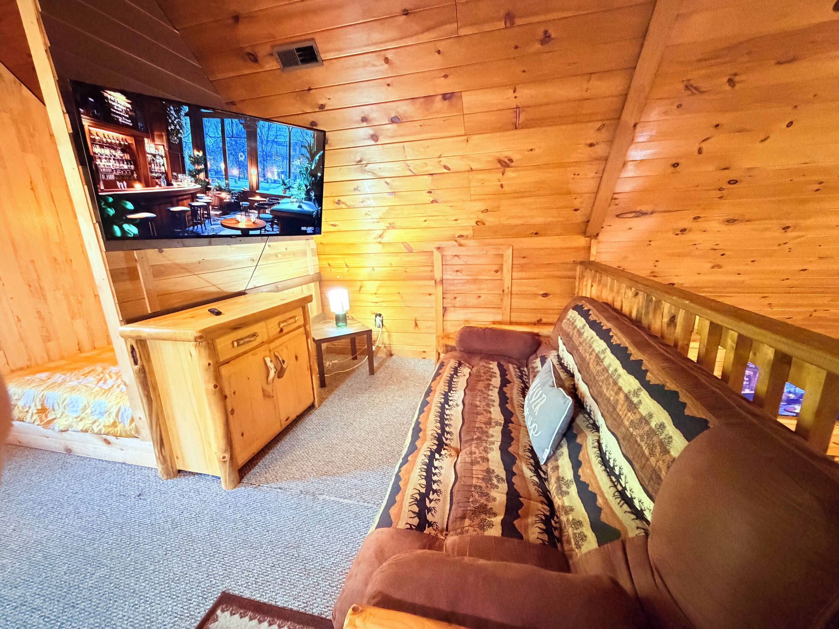 A cozy cabin interior with a wooden wall, a sofa, a television, and a small table.