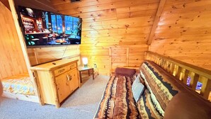 Interior acolhedor de uma cabana com parede de madeira, um sofá, uma televisão e uma mesa pequena.