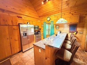 A kitchen with wooden cabinets, stainless steel appliances, a bar area with stools, and a hanging light fixture. - 2 King Suites + Loft with 4 Full Beds | Hot Tub | Resort Pool (Sevierville)