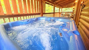 Uma banheira de hidromassagem em uma cabana de madeira, com um deck de madeira e vista para o verde lá fora.