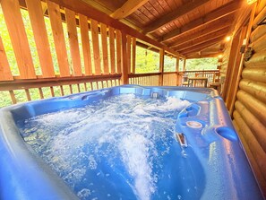 A hot tub in a wooden cabin with a wooden deck and a view of greenery outside. - 2 King Suites + Loft with 4 Full Beds | Hot Tub | Resort Pool (Sevierville)