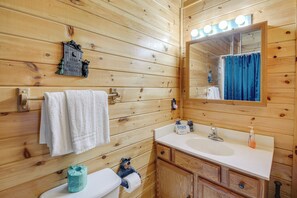 Ein Badezimmer einer Holzhütte mit einem weißen Waschbecken, einem Spiegel mit Beleuchtung und einem Handtuchhalter.