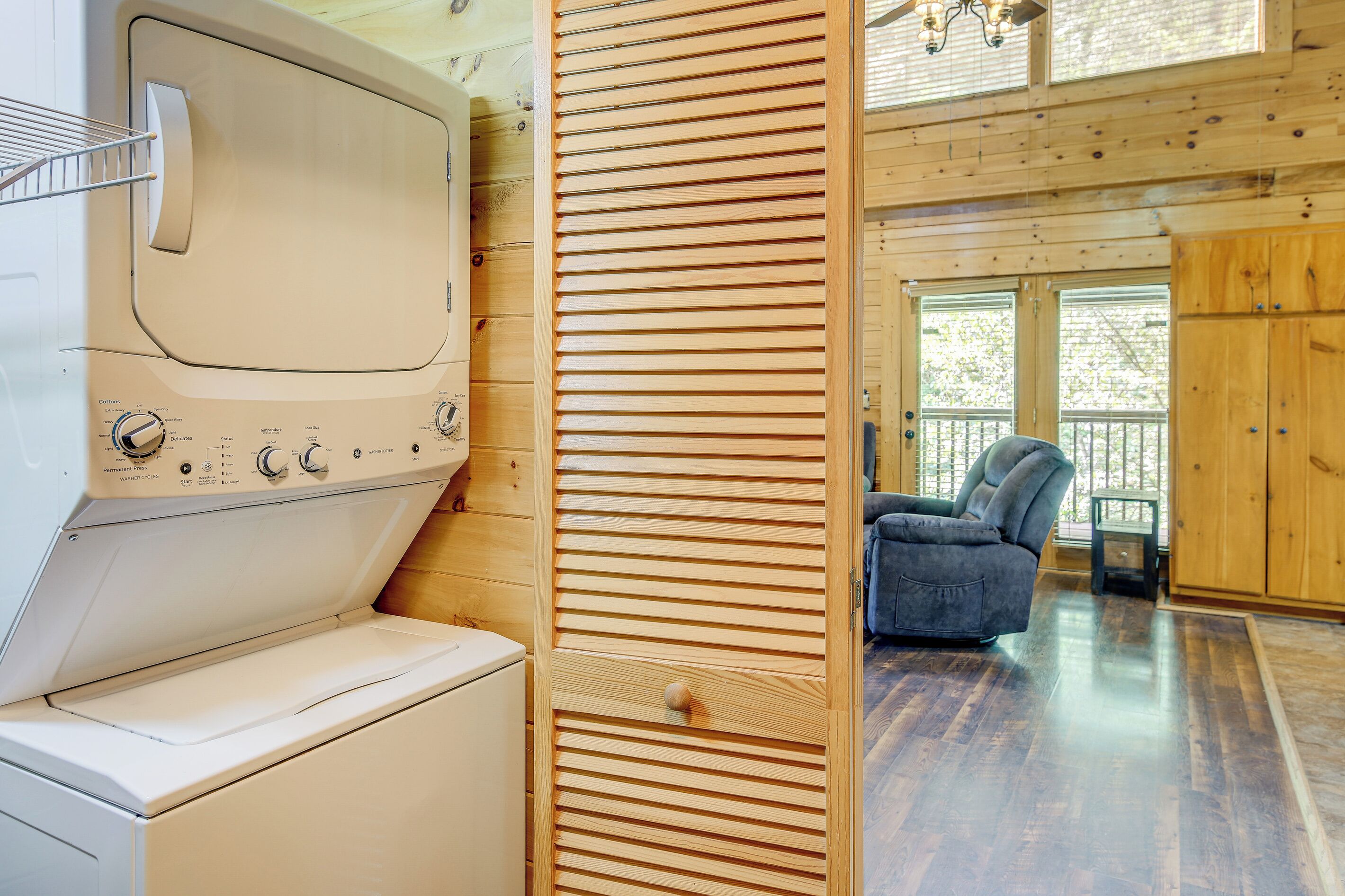 A laundry area with a washing machine and dryer, a wooden sliding door, and a view of a balcony with a chair.