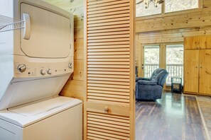 A laundry area with a washing machine and dryer, a wooden sliding door, and a view of a balcony with a chair. - 2 King Suites + Loft with 4 Full Beds | Hot Tub | Resort Pool (Sevierville)