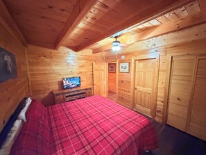A wooden cabin room with a bed, a television, and a ceiling fan. - 2 King Suites + Loft with 4 Full Beds | Hot Tub | Resort Pool (Sevierville)