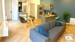 Ein modernes Wohnzimmer mit einer Couch, einem Glastisch und einer Küchenzeile mit Schränken und Geräten.