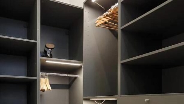 Ein begehbarer Kleiderschrank mit mehreren Regalen und Ablageflächen, mit einem Fischgrätparkettboden.