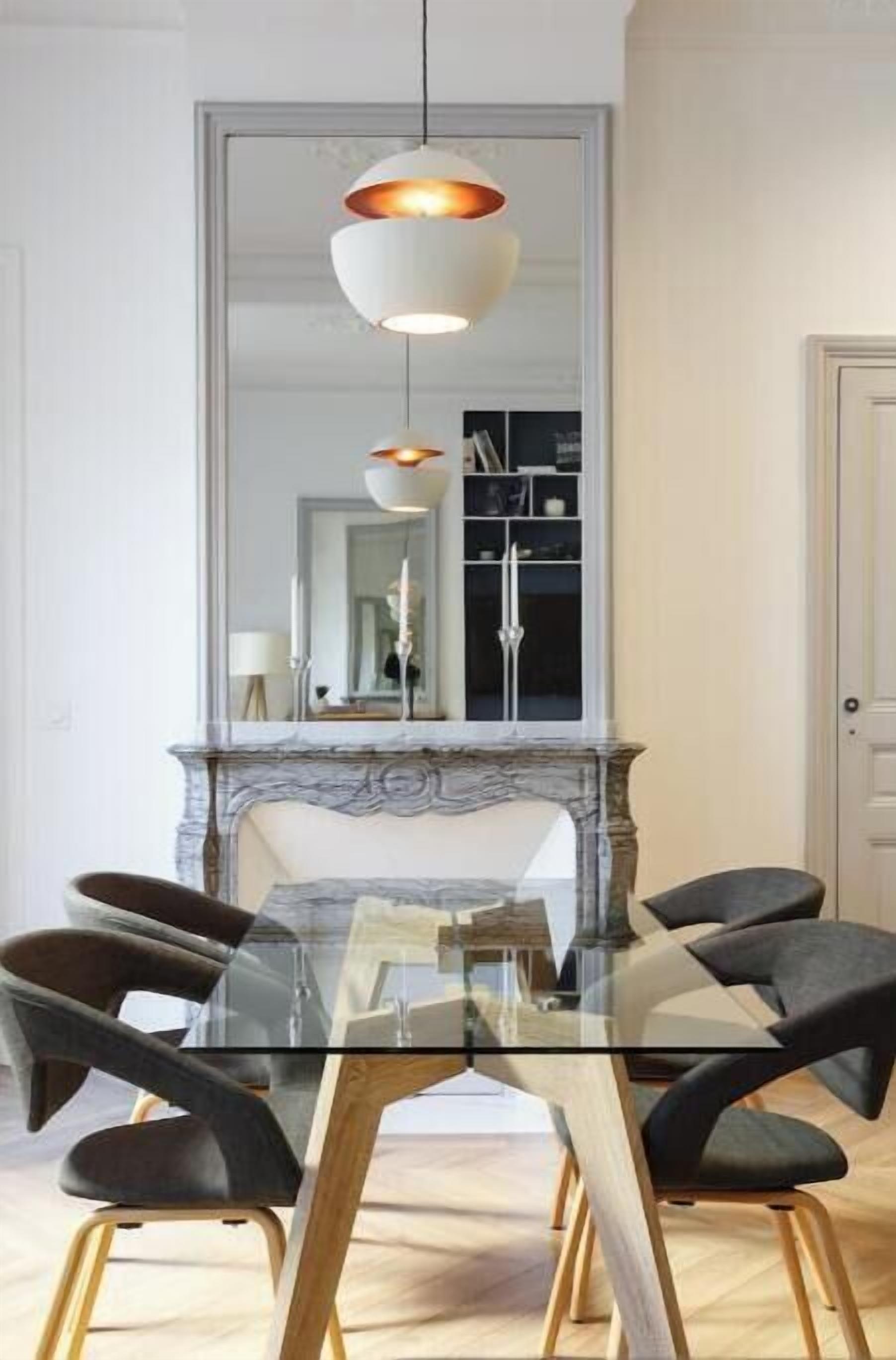 A dining area with a glass table, black upholstered chairs, and a marble fireplace.