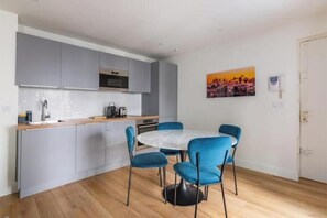 A compact kitchen with grey cabinets, a white countertop, and a round table with blue chairs. - Renovated apartment between the Opera and the Louvre (Île-de-France)