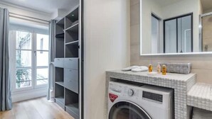 Ein modernes Badezimmer mit integrierter Waschmaschine, einem großen Spiegel und Blick auf einen Balkon.