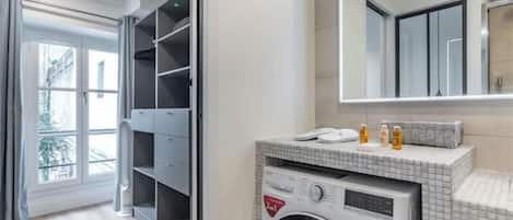 Uma casa de banho moderna com máquina de lavar embutida, um espelho grande e vista para uma varanda.