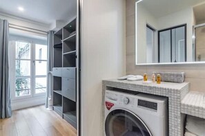 A modern bathroom with a built-in washing machine, a large mirror, and a view of a balcony. - Renovated apartment between the Opera and the Louvre (Île-de-France)