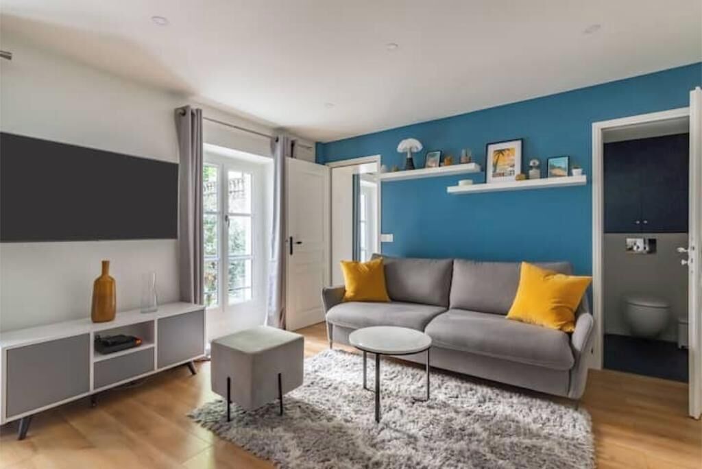 Un salon moderne avec un canapé gris, une petite table d’appoint blanche et une étagère grise.