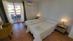 A hotel room with two beds, a chair, a lamp, and a view of the outside. - El Rincon 12 - One Bed (Los Cristianos)