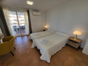 Ein Hotelzimmer mit zwei Betten, einem Sessel, einer Lampe und Blick ins Freie.