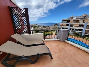 Ein Balkon mit zwei Loungestühlen, einem Pool und Blick auf Gebäude sowie das Meer.